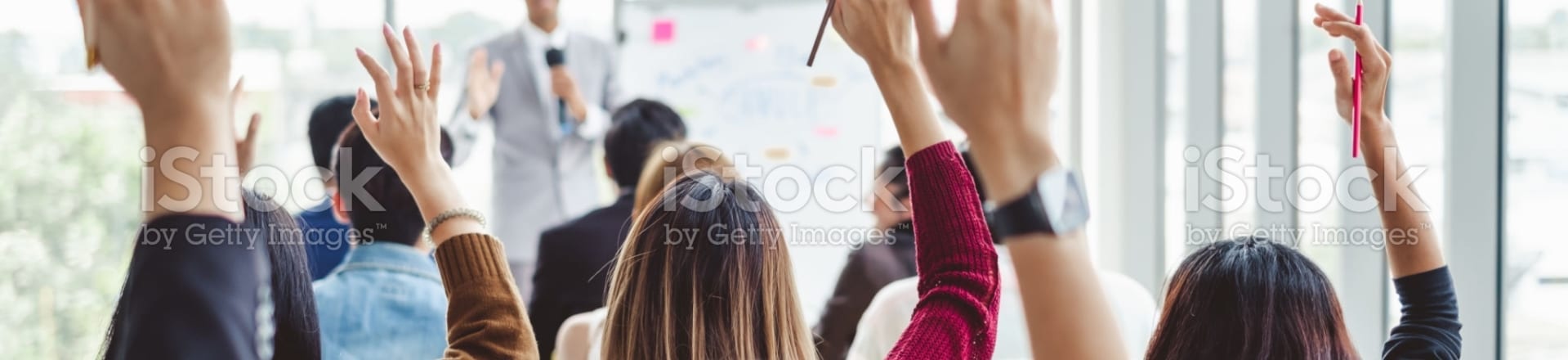 Plusieurs personnes de dos levant la main devant quelqu'un donnant une présentation