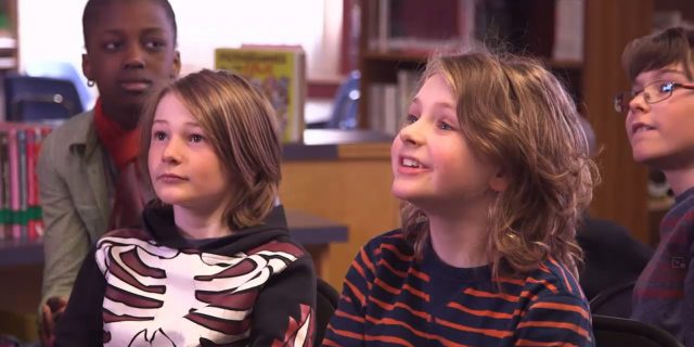 Jeunes de l'élémentaire dans une classe écoutant quelqu'un