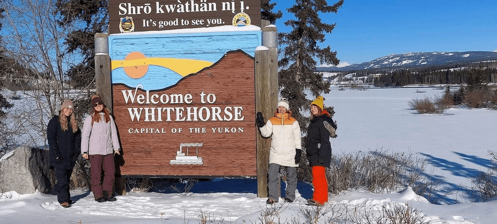 Stagiaires devant une pancarte disant Welcome to WHITEHORSE devant une paysage hivernal